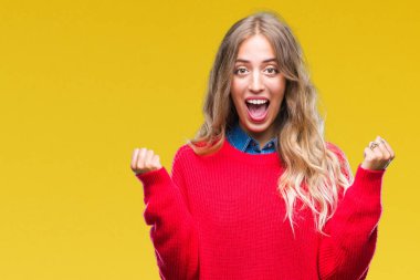 İzole arka plan üzerinde kutluyor kış kazak giyen güzel genç sarışın kadın şaşırttı ve başarı için kaldırdı kollarını açarak hayret ve gözleri açık. Kazanan kavramı.