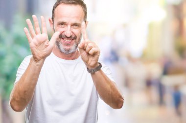 Orta yaş ağarmış komuta sizde gösterilen ve parmakları ile işaret izole arka plan üzerinde beyaz t-shirt giyen süre kendinden emin ve mutlu gülümseyerek 6 numara.
