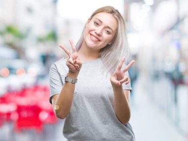 Genç Sarışın kadın parmaklarını zafer işareti yaparken gösterilen kamera seyir gülümseyen izole arka plan yüzünden. İki numaralı.