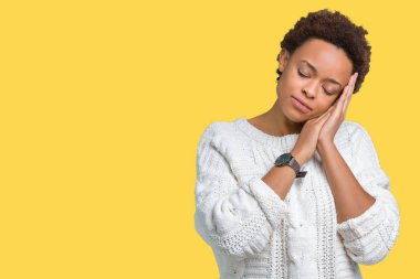 Uyku yorgun hayal ve ellerle birlikte poz ile kapalı gözler gülümseyen izole arka plan üzerinde kazak giyen güzel genç Afro-Amerikan kadın.
