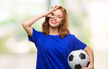 Mutlu yüz el parmaklarının arasından seyir göz üzerinde ok işaretiyle yapıyor gülümseyen ile futbol futbol topu tutan izole arka plan üzerinde genç güzel kadın