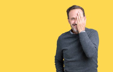 Yakışıklı orta yaş komuta sizde bir göz ile yüz ve sürpriz duygu kendinden emin gülümseme ile el kapsayan izole arka plan üzerinde bir kazak giyiyor.