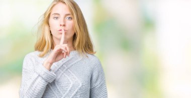 Dudaklarında parmak ile sessiz olmanı izole arka plan üzerinde kış kazak giyen güzel genç kadın. Sessizlik ve gizli kavramı.