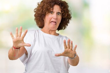 Şokta bağırarak korkuyor ve dehşet korku ifade dur hareketi el ile ile izole arka plan üzerinde beyaz t-shirt giyen güzel orta ager kadın kıdemli. Panik kavramı.