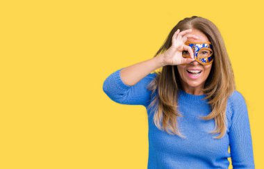 Güzel orta yaş kadın giyiyor Venedik Karnavalı maskeyi gülümseyen, parmakları ile mutlu yüz üzerinden seyir göz el ile ok jest yapıyor izole arka plan üzerine.