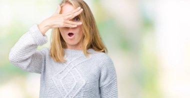 Mahcup ifadeyle parmaklarımın arasından seyir yüz ve gözler el ile kapsayan şok izole arka plan bakmak üzerinde kış kazak giyen güzel genç kadın.