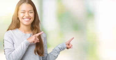 Gülümseyen ve iki elleri ve parmakları ile tarafına işaret kamera bakarak izole arka plan üzerinde kazak giyen genç güzel esmer kadın.