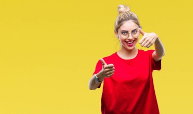 El ile pozitif jest yapıyor onaylama izole arka plan üzerinde kırmızı t-shirt ve gözlük giyen genç güzel sarışın kadın başparmak gülümseyen ve başarı için mutlu. Kamera, kazanan jest arıyorsunuz.