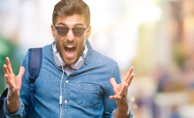 Üzerinde kulaklık ve sırt çantası giyen genç yakışıklı turist adam deli kutluyor arka plan izole ve başarı için kaldırdı kollarını açarak hayrete ve heyecanlı çığlık gözleri açık. Kazanan kavramı