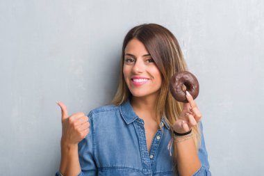 Genç Yetişkin kadın işaret ve başparmak kadar mutlu yüz gülümseyen tarafı ile gösterilen çikolatalı çörek yeme gri grunge duvarın üzerinden