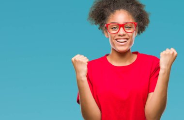 İzole arka plan üzerinde kutluyor gözlük takan genç afro Amerikalı kadın şaşırttı ve silah ile başarı için yükseltilmiş ve açık gözler hayrete düşürdü. Kazanan kavramı.
