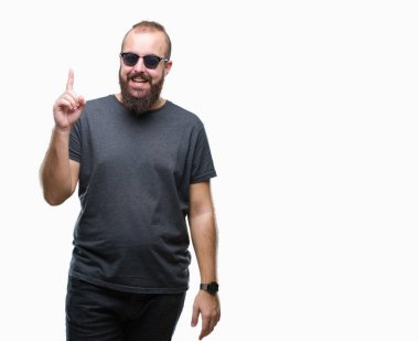 Genç beyaz hipster adam başarılı fikirle izole arka plan işaret parmağı üzerinde güneş gözlüğü takıyor. Çıktıktan ve mutlu. Bir numara.