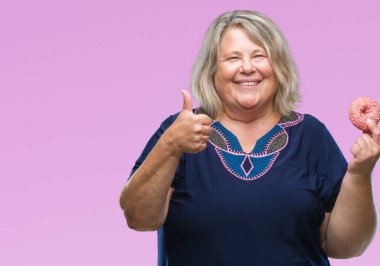 Üst düzey plus kafkas kadın yeme şeker çörek izole arka plan üzerinde mutlu ok işareti yapıyor büyük gülümseme ile boyutu, parmaklarıyla, mükemmel işaret parmak