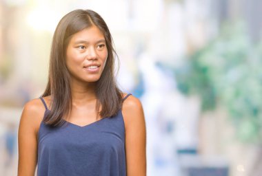 Genç Asyalı kadın uzak tarafına yüzünde, doğal ifade gülümseme ile seyir izole arka plan üzerinde. Kendine güvenen gülüyor.