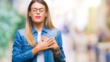 Gözlük ile gülümseyen izole arka plan üzerinde genç güzel kadın kapalı gözler ve yüzünde minnettar jest ile göğüs üzerinde eller. Sağlık kavramı.