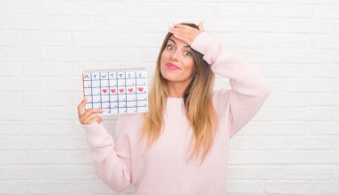 Dönem takvim kafasına, el ile vurguladı holding beyaz tuğla duvarın üzerinden Genç Yetişkin kadın şok utanç ve sürpriz suratla, öfkeli ve sinirli. Korku ve hata için üzgün.