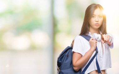 Genç Asyalı kadın giyiyor sırt çantası ve kamera ve size parmak ile işaret izole arka plan üzerinde kulaklık, el işareti, pozitif ve kendinden emin bir jest ön