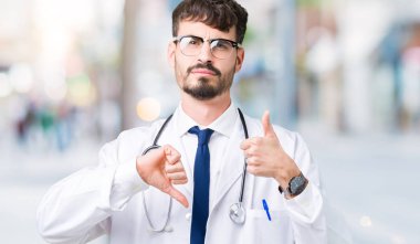 Genç izole arka plan yapmaya başparmak yukarı ve aşağı, anlaşmazlık ve anlaşma ifade üzerinde hastane ceket giyen adam doktor. Deli çatışma