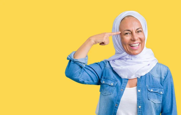 Middle age eastern arab woman wearing arabian hijab over isolated background Smiling pointing to head with one finger, great idea or thought, good memory