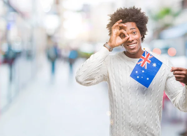 アフロ アメリカ人が指を通して見る目に手で サインをして笑っている幸せそうな顔で孤立した背景にオーストラリアのフラグします — ストック写真