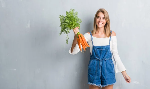 Vacker Ung Kvinna Över Grunge Grå Väggen Håller Färska Morötter — Stockfoto