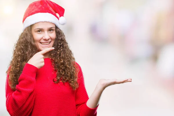 年轻的黑发女孩在孤立的背景上戴着圣诞帽 惊讶地对着镜头微笑 同时用手和手指指指点点 — 图库照片