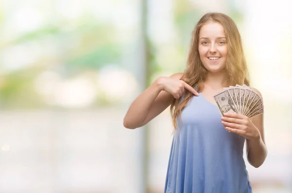 Joven Mujer Rubia Sosteniendo Dólares Con Cara Sorpresa Señalando Dedo — Foto de Stock