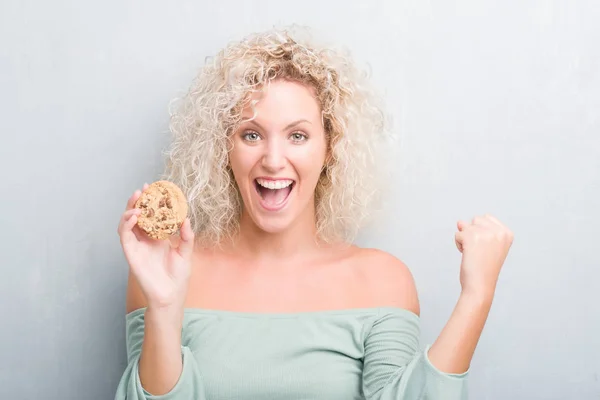 Young Blonde Woman Grunge Grey Wall Eating Chocolate Chip Cooky — Stock Photo, Image