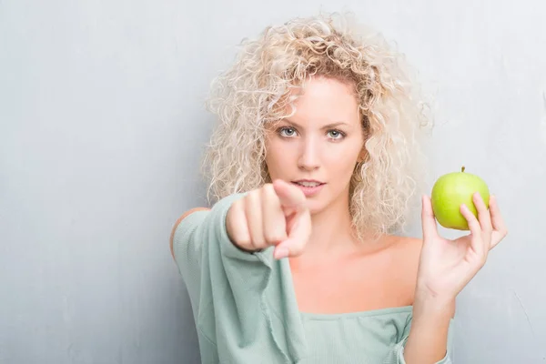 Young Blonde Woman Grunge Grey Background Eating Green Apple Pointing — Stock Photo, Image