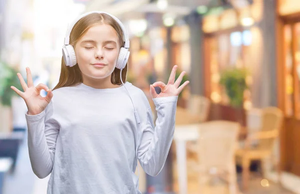 年轻美丽的女孩戴着耳机听音乐在孤立的背景下放松和微笑闭上眼睛做冥想手势用手指 瑜伽理念 — 图库照片