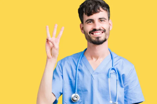 年轻英俊的护士男子穿着外科医生制服在孤立的背景显示和手指第三 而微笑着自信和快乐 — 图库照片