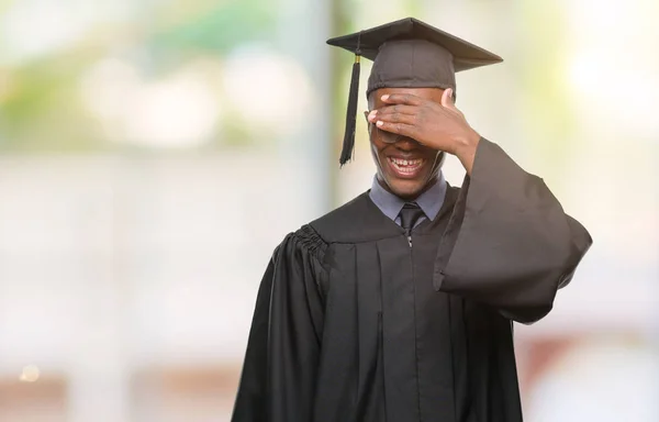 Young graduated african american man over isolated background smiling and laughing with hand on face covering eyes for surprise. Blind concept.