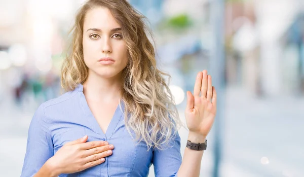 Beautiful young blonde business woman over isolated background Swearing with hand on chest and open palm, making a loyalty promise oath