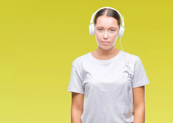 年轻的白种人妇女听音乐戴着耳机在孤立的背景与严重的表情在脸上 简单而自然地看着相机 — 图库照片