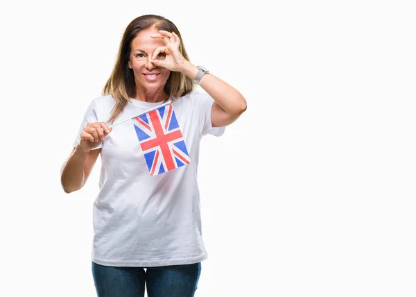 中年西班牙妇女拿着英国的旗子在孤立的背景与愉快的面孔微笑做确定的标志用眼睛看着通过手指 — 图库照片