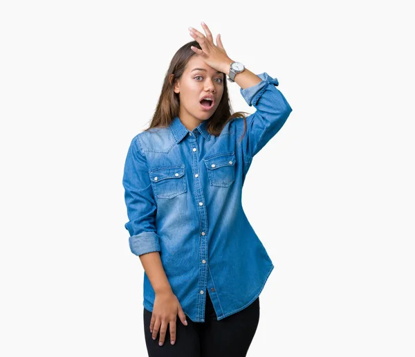 年轻美丽的黑发女人穿着蓝色粗斜纹棉布衬衫在孤立的背景惊讶与手在头上的错误 记住错误 糟糕的记忆概念 — 图库照片