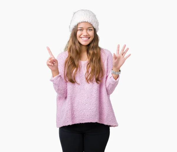 若い美しいブルネットの女性の身に着けているセーターと分離の背景表示と指で上向きに冬帽子が自信を持って 幸せな笑みを浮かべている間ナンバーシックスします — ストック写真