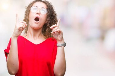 Güzel esmer kıvırcık saçlı Genç kız izole arka plan üzerinde gözlük hayret ve yukarıya bakıp parmakları ile işaret şaşırttı ve silah kaldırdı.