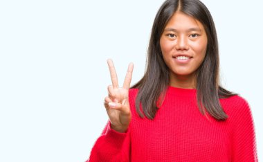 Genç Asyalı kadın giyiyor kış kazak gösterilen ve parmakları ile işaret izole arka plan üzerinde ikincisi ise kendinden emin ve mutlu gülümseyerek.