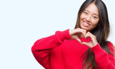 Genç Asyalı kadın kalp simgesi ve elleriyle şekil gösterilen aşık gülümseyen izole arka plan üzerinde kış kazak giyiyor. Romantik kavramı.