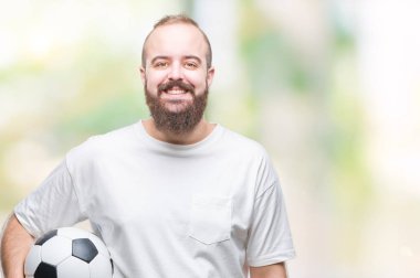 Futbol futbol topu ayakta ve diş gösterilen kendine güvenen bir gülümsemeyle gülümseyerek mutlu bir yüz ile izole arka plan üzerinde tutan genç beyaz hipster adam
