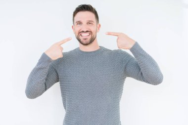 Genç yakışıklı adam kendinden emin gösterilen ve işaret parmakları diş ve ağız ile gülümseyen izole arka plan üzerinde rahat kazak giyiyor. Sağlık kavramı.