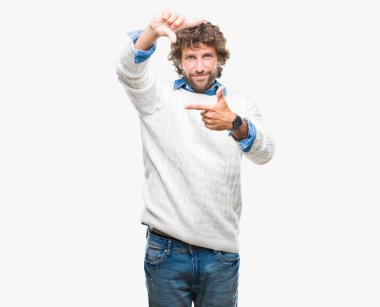Yakışıklı İspanyol adam elleriyle yapım çerçeve ve parmakları ile mutlu yüz gülümseyen izole arka plan üzerinde giyen kış kazak modeli. Yaratıcılık ve Fotoğrafçılık kavramı.