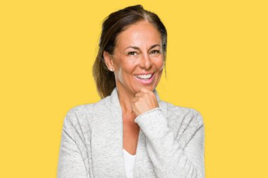 Emin çapraz kollar ve çeneme kaldırdı el ile gülümseme ile kameraya bakarak izole arka plan üzerinde kış kazak giyen güzel orta yaş yetişkin kadın. Pozitif düşünce.