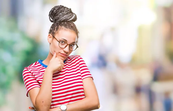Young braided hair african american girl wearing glasses over isolated background with hand on chin thinking about question, pensive expression. Smiling with thoughtful face. Doubt concept.
