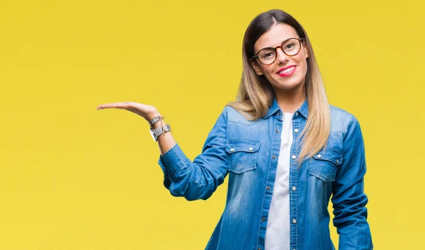 Young beautiful woman over wearing glasses over isolated background smiling cheerful presenting and pointing with palm of hand looking at the camera.