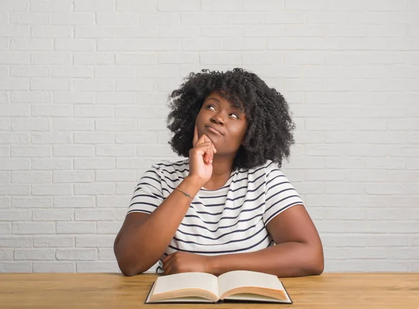 Mujer Afroamericana Joven Sentada Mesa Leyendo Libro Cara Seria Pensando —  Fotos de Stock
