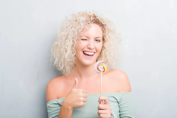 Młoda Blondynka Nad Grunge Szara Ściana Jedzenie Candy Lollipop Szczęśliwy — Zdjęcie stockowe