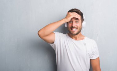 Yakışıklı genç adam kafasına, el ile vurguladı müzik dinlerken kulaklık giyen gri grunge duvarın üzerinden şok utanç ve sürpriz suratla, öfkeli ve sinirli. Korku ve hata için üzgün.