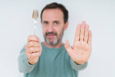 Komuta sizde açık eliyle dur işareti ile ciddi ve kendine güvenen ifade, savunma jest yapıyor izole arka plan üzerinde gümüş çatal tutan